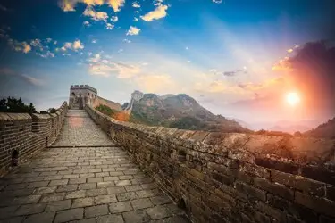 Great Wall of China at sunrise, stone walkway stretching across mountain ridges under golden light.