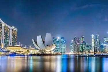 Singapore skyline at night featuring Marina Bay Sands and the ArtScience Museum reflected across Marina Bay waters.