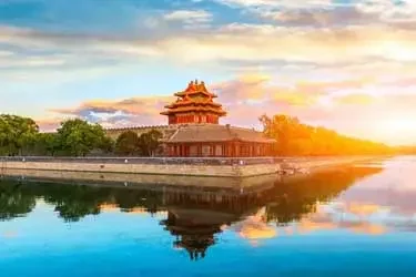 Corner tower of the Forbidden City reflected in the surrounding moat at sunset in Beijing, China