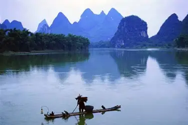 Fisherman on a bamboo raft along the Li River in Guilin, framed by iconic karst mountains and calm waters.