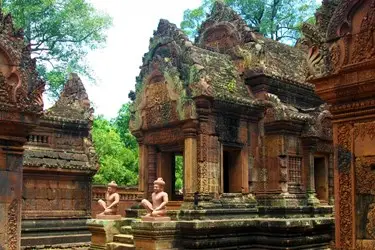 Intricately carved red sandstone temple ruins at Banteay Srei in Angkor, Cambodia, surrounded by lush forest and known for its detailed Khmer architecture.