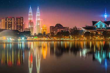 Kuala Lumpur skyline at night featuring the Petronas Twin Towers, illuminated city lights reflected in KLCC Park lake, Malaysia.