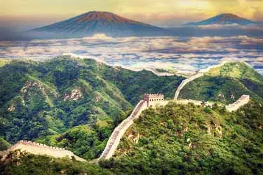 The Great Wall of China winding across forested mountain ridges at sunrise, highlighting ancient watchtowers and dramatic northern China landscapes.