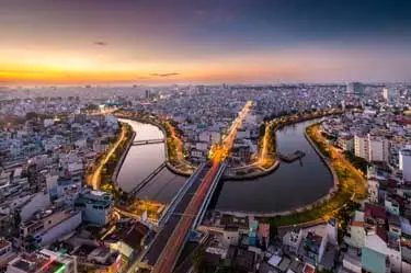 Aerial view of Ho Chi Minh City at sunset with winding waterways and illuminated boulevards, showcasing Vietnam’s dynamic urban landscape.