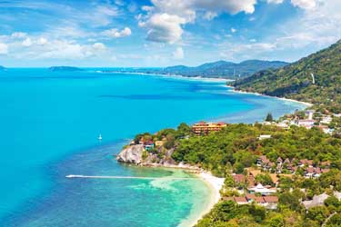 Aerial view of Phuket’s coastline in Thailand, showcasing sweeping sandy beaches, turquoise Andaman Sea waters, hillside resorts, and lush tropical scenery.