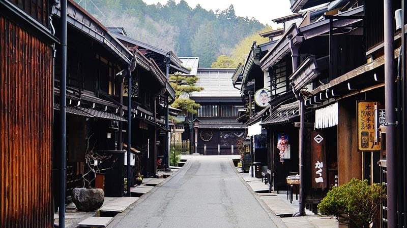Quiet street in Takayama’s old town lined with traditional wooden merchant houses, with mountains rising in the background.