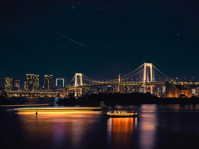 Night view of Tokyo’s Rainbow Bridge illuminated over Tokyo Bay with city lights and boats reflecting on the water