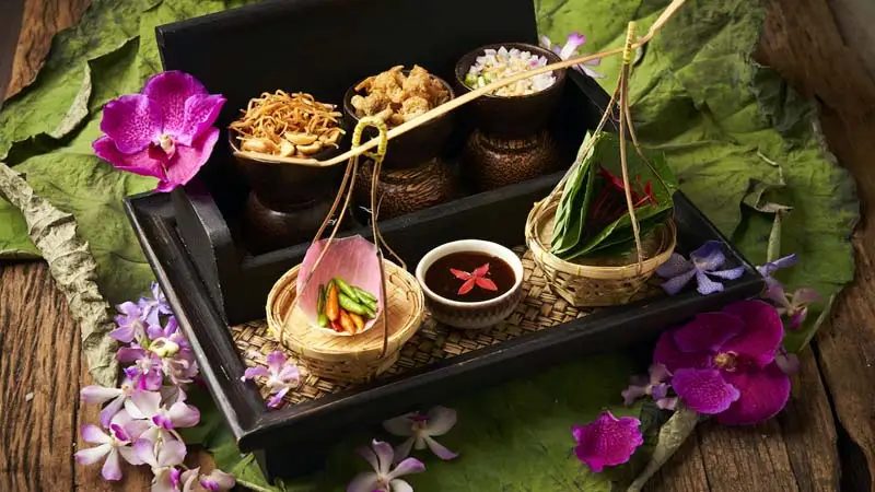 Assorted Thai dishes and condiments elegantly arranged on a tray with small bowls, fresh herbs, and colorful garnishes set on a banana leaf background.