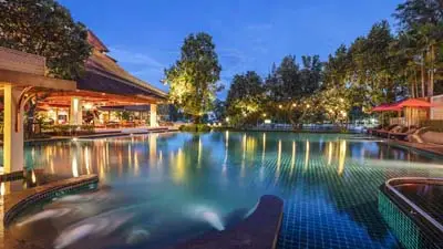 Ratilanna Riverside Resort in Chiang Mai featuring an illuminated riverside swimming pool, elegant Lanna-style architecture, and a tranquil setting conveniently located near the city center.