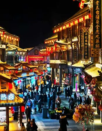 Lantern-lit pedestrian street in Lijiang Old Town at night, showcasing traditional architecture, shops, and vibrant evening atmosphere.