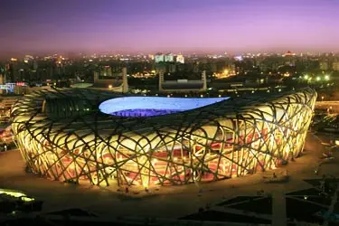 Beijing National Stadium (Bird’s Nest) illuminated at night in Beijing, China, showcasing its iconic lattice architecture against the city skyline at dusk.