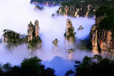 Sandstone pillars of Zhangjiajie rising through mist, showcasing the dramatic mountain scenery of Hunan, China.