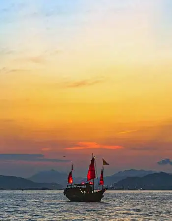 Traditional junk boat sailing at sunset on coastal waters, evoking timeless maritime scenes found along Hong Kong’s historic waterways.