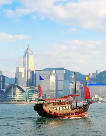 Traditional junk boat sailing across Victoria Harbour in Hong Kong with the modern skyline in the background.