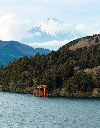 Mount Fuji rising above Lake Ashi with a torii gate along the shoreline in Hakone