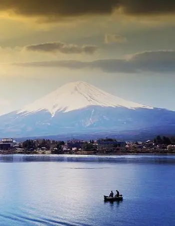 Mount Fuji rising above Lake Kawaguchi at sunrise, with a traditional fishing boat on the water, showcasing one of Japan's most iconic natural landscapes.