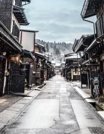 Takayama's preserved merchant quarter with lantern-lit alleyways and wooden storefronts dusted in snow, evoking centuries past