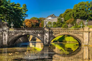 Nijubashi Bridge at Tokyo’s Imperial Palace, with stone arches reflected in the palace moat amid landscaped gardens and seasonal foliage.