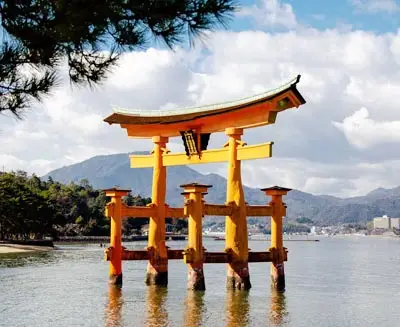 Sacred torii gate rising from the water near Miyajima with mountains in the background