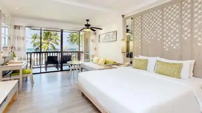 Bright guest room at Katathani Phuket Beach Resort, featuring tropical décor, a king bed, and a private balcony overlooking palm trees near Kata Beach.