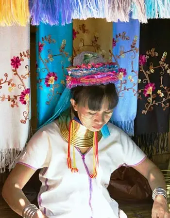 Kayan (Padaung) woman in northern Thailand wearing traditional brass neck rings and colorful woven headwear, representing hill tribe culture and craftsmanship.
