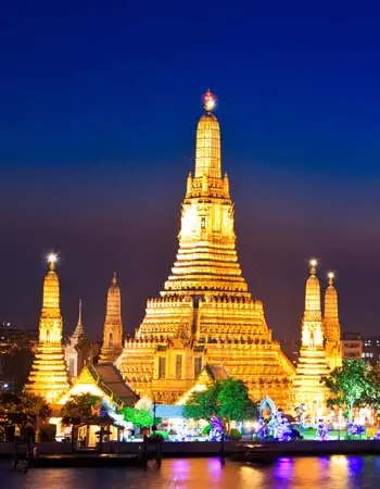 Wat Arun (Temple of Dawn) illuminated at night in Bangkok, Thailand, with its towering central prang and glowing spires reflecting along the Chao Phraya River.
