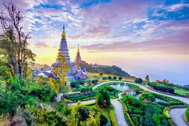 Wat Phra That Doi Inthanon in Chiang Mai, Thailand, at sunrise, featuring golden pagodas, landscaped gardens, and mountain views under a colorful sky.