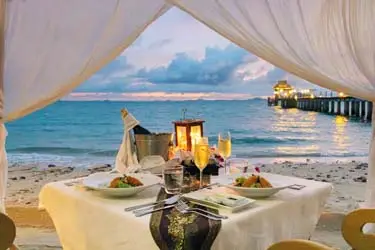 Romantic beachfront dining setup on Koh Yao Yai, Thailand, with candlelit table, ocean views, and a pier extending into the Andaman Sea at dusk.