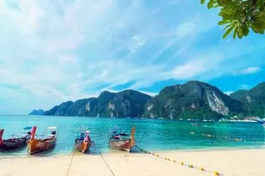 Long-tail boats moored along the shore in Krabi, Thailand, with turquoise waters and dramatic limestone cliffs rising from the Andaman Sea.