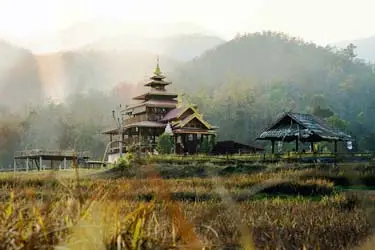 Traditional wooden temple and rural structures in Pai, Thailand, set amid misty hills and golden fields in the peaceful northern countryside.