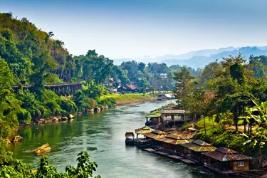 Floating lodges along the River Kwai in Kanchanaburi, Thailand, with wooden bungalows set against lush jungle hills and calm river scenery.