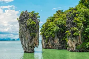 Limestone karst formations rising from emerald-green waters in Phang Nga Bay, Thailand, surrounded by lush tropical vegetation and calm coastal scenery.