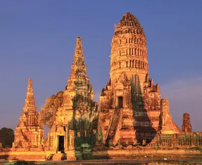 Ancient temple ruins of Ayutthaya, Thailand, featuring towering prang-style structures built from weathered brick and stone, glowing in warm evening light.