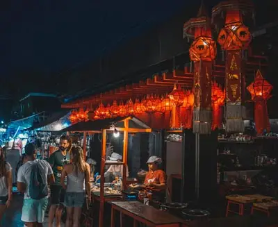 Chiang Mai night market with lantern-lit stalls, local vendors, and visitors browsing handicrafts and street food in a lively evening atmosphere.