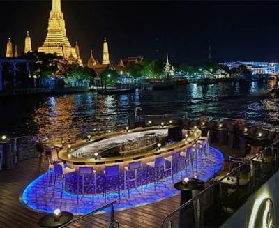 Dinner cruise on the Chao Phraya River in Bangkok, featuring an open-air dining deck with illuminated seating and nighttime views of Wat Arun and riverside landmarks.