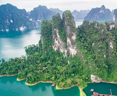 Limestone karst cliffs rising above emerald-green waters in Khao Sok National Park, southern Thailand, surrounded by dense rainforest and dramatic mountain scenery.