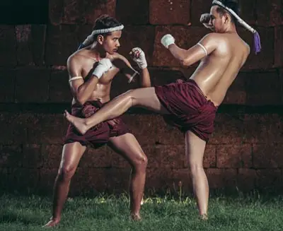 Traditional Muay Thai fighters practicing a kicking technique, showcasing Thailand’s national martial art with classic attire and disciplined combat form.