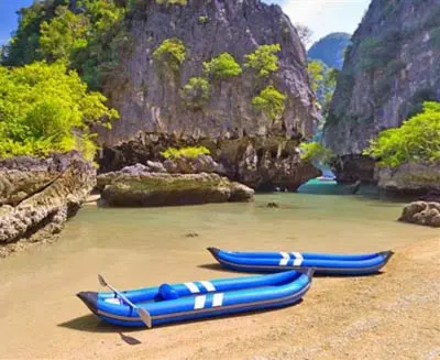 Kayaks resting on a sandy beach in Krabi, Thailand, framed by dramatic limestone cliffs and calm turquoise water in a secluded coastal lagoon.