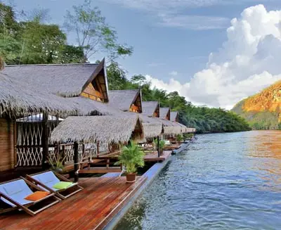 Riverside floating bungalows in Kanchanaburi, Thailand, featuring thatched-roof lodges, wooden decks, and tranquil river views surrounded by lush jungle scenery.