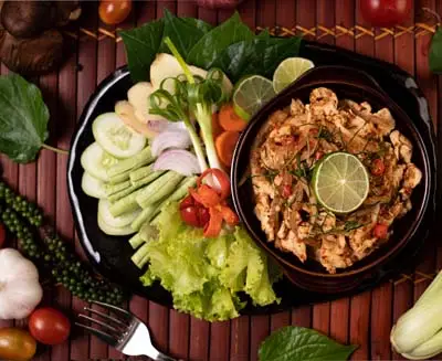 Thai cooking class featuring freshly prepared minced chicken with lime and herbs, served with crisp vegetables and traditional ingredients on a rustic table.