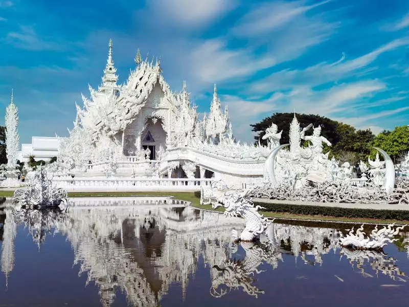 Ornate Wat Rong Khun with mirrored water reflection — upscale cultural sightseeing in Chiang Rai, Thailand
