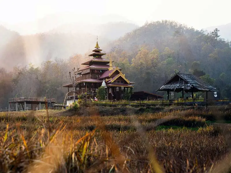 Shan-inspired wooden temple framed by mountain haze and quiet farmland in Mae Hong Son province