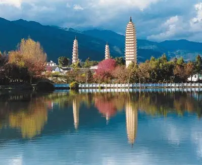 Three Pagodas of Chongsheng Temple in Dali reflected on a tranquil lake, with Cangshan Mountains rising behind this iconic Yunnan landmark.
