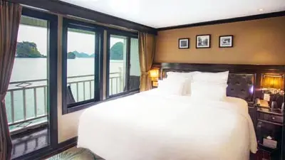 Comfortable cabin aboard Paradise Sails Cruise on Ha Long Bay, Vietnam, featuring large windows, private balcony access, and serene views of limestone karsts and calm emerald waters.