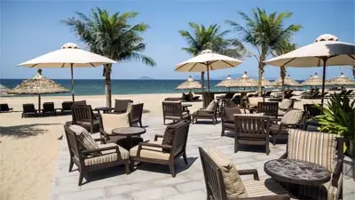 Beachfront seating at Hoi An Boutique Resort, featuring shaded lounge chairs and umbrellas on a quiet sandy beach, framed by palm trees and open ocean views.