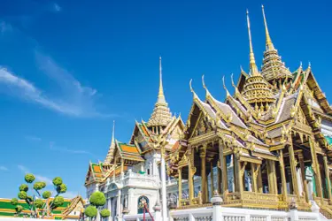 Wat Phra Kaew (Temple of the Emerald Buddha) in Bangkok, Thailand, featuring ornate golden spires and intricate traditional Thai architecture under a clear blue sky.