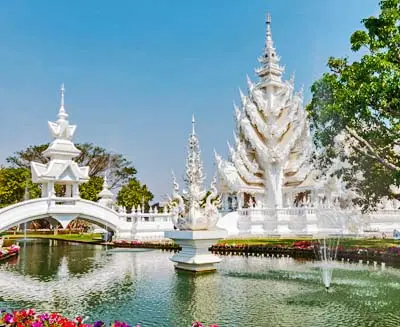 Wat Rong Khun (White Temple) in Chiang Rai, Thailand, showcasing intricate white carvings, ornate spires, and reflective pools under a clear blue sky.