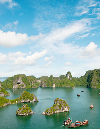 Traditional wooden junks cruising through the emerald waters of Ha Long Bay, Vietnam, surrounded by dramatic limestone karsts in this UNESCO World Heritage seascape.
