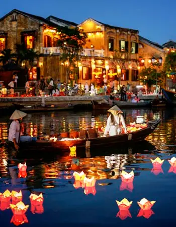 Traditional lantern boat floating on the Thu Bon River in Hoi An Ancient Town, Vietnam, with glowing paper lanterns reflecting on the water and historic riverside buildings illuminated at night.