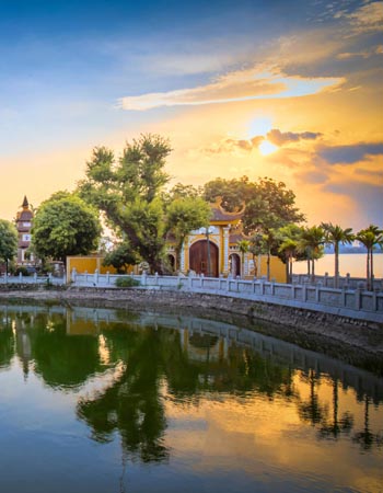 Sunset view of Tran Quoc pagoda reflected in a calm lake in Vietnam, with golden evening light illuminating traditional architecture and surrounding trees.